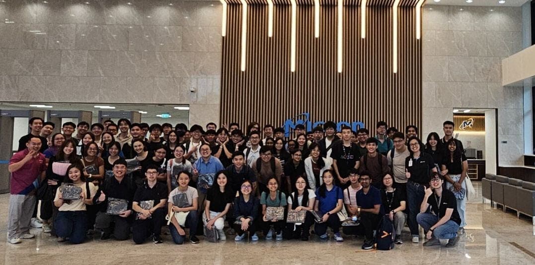 The full group of student visitors photographed in the lobby beneath the Micron sign