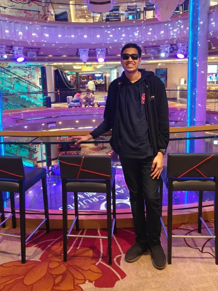Nooka Satyendra in sunglasses, leaning on a glass railing in a cruise ship's atrium